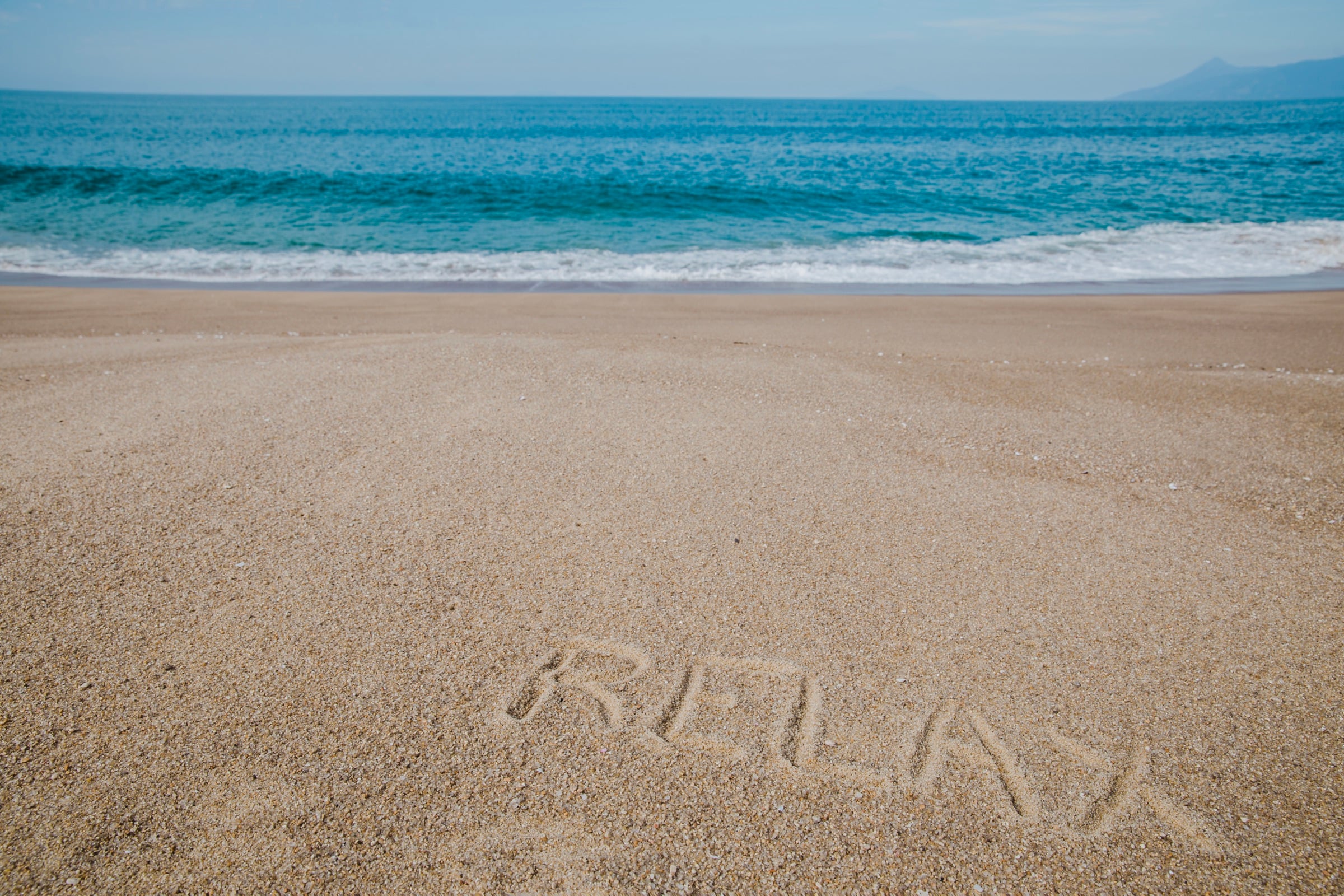 The word RELAX written in the sand with the ocean behind it