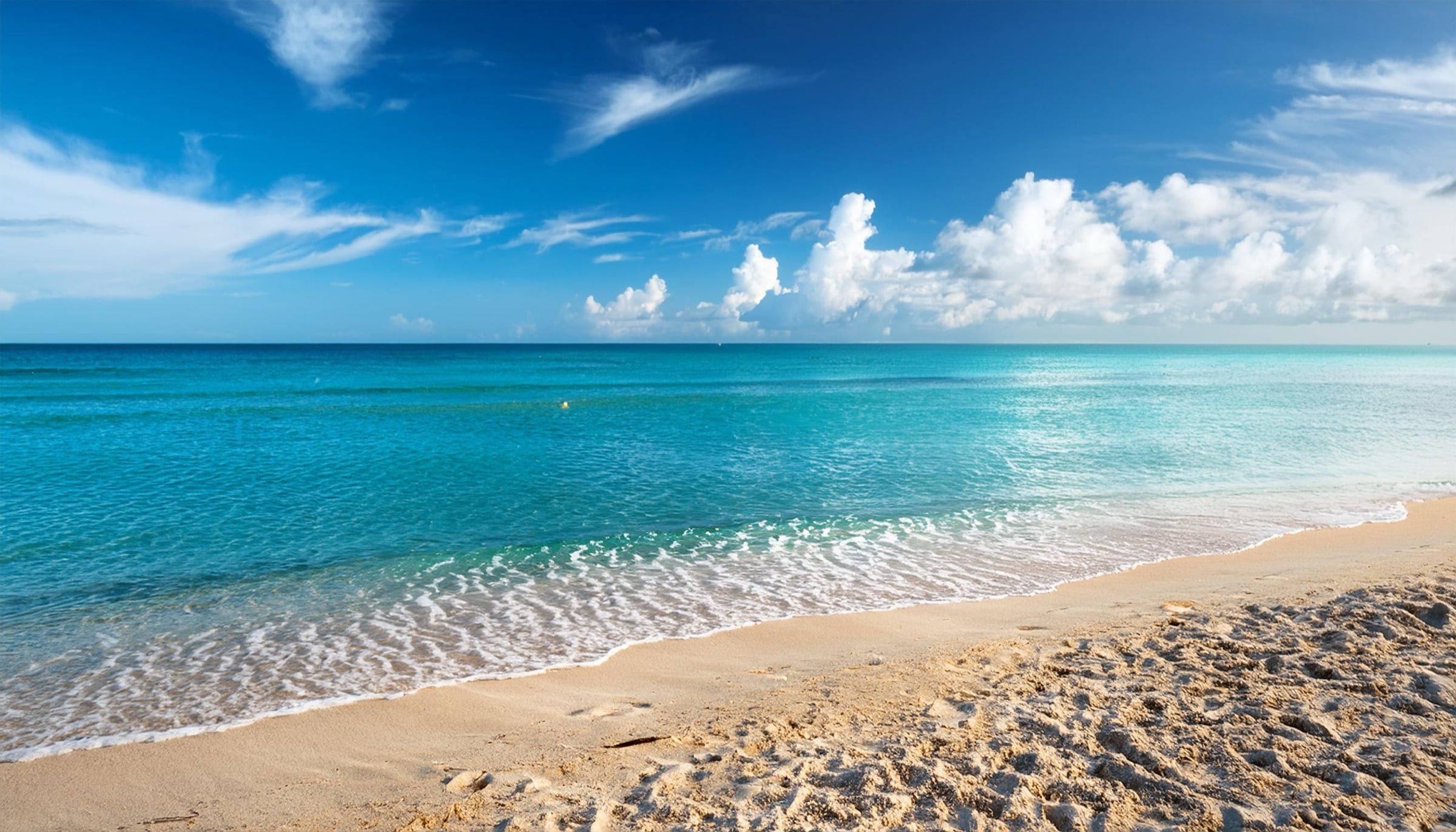 Turquoise waves rolling onto a golden beach under a deep blue sky