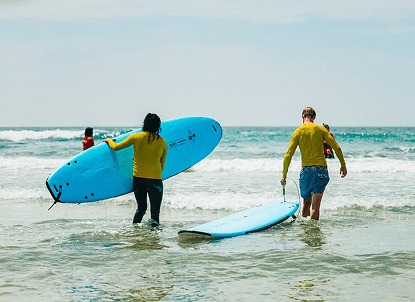 Two people carrying blue surfboards into the shallows